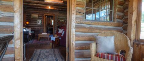 Ein Holzblockhaus-Innenraum mit einem Korbstuhl, einem roten Sofa und einem Holztisch.