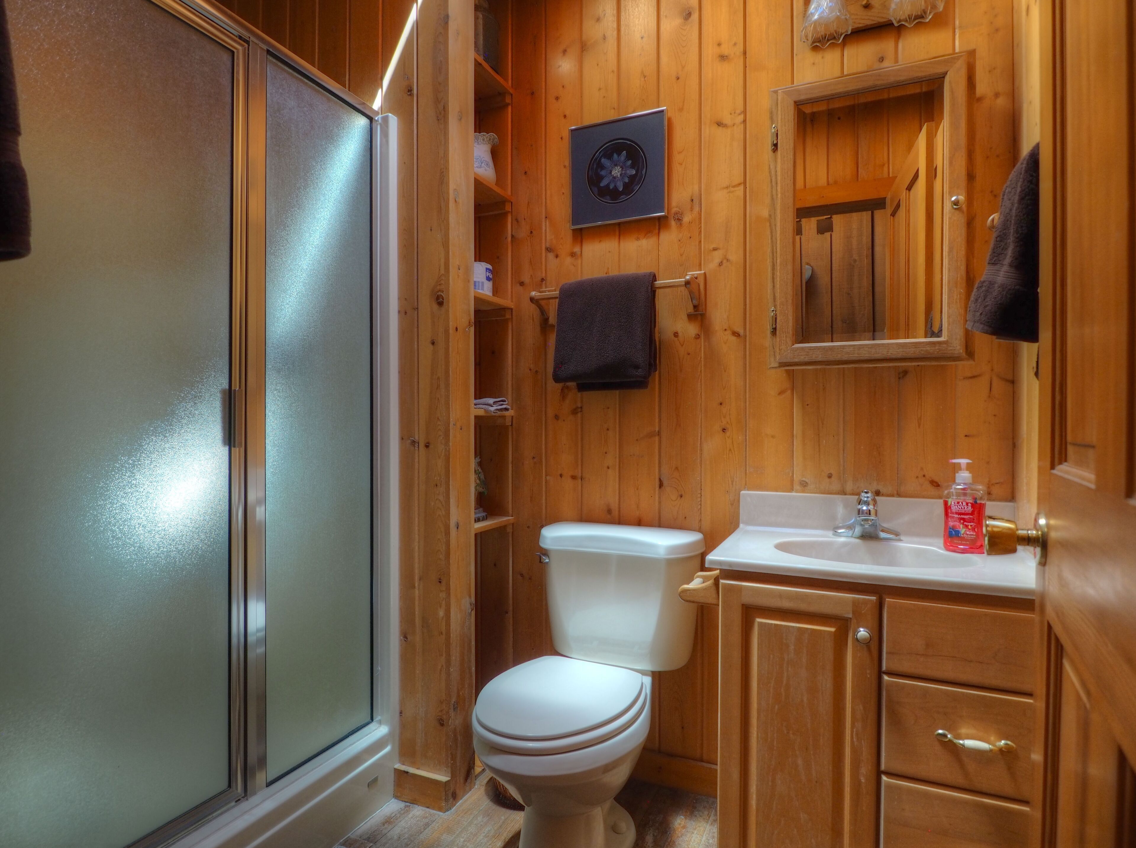 A wooden bathroom with a toilet, sink, and shower.