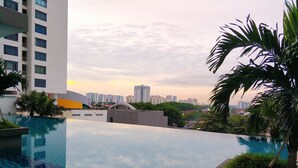 Una piscina infinita en la azotea con vistas a un paisaje urbano, rodeada de vegetación y edificios modernos.