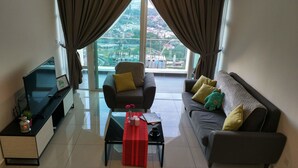 Una sala moderna con sofá, sillón y una mesa de centro. Hay un televisor sobre un mueble bajo y una ventana con cortinas.