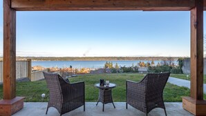 A covered patio with two wicker chairs and a small table, overlooking a body of water and a distant shoreline. - Pier View Suite, Stunning Ocean View. (Campbell River)