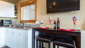 A modern kitchen with a built-in oven, a large flat-screen TV, and a dining area with bar stools. - Pier View Suite, Stunning Ocean View. (Campbell River)
