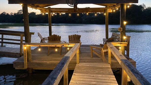 A wooden deck with chairs and string lights, overlooking a calm body of water. - Shem Creek Paradise. Fish, Paddle, Kayak Off Your Own Covered dock with floater (Mt Pleasant)