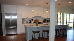 A modern kitchen with white cabinets, a stainless steel refrigerator, wooden stools, and pendant lighting. - Shem Creek Paradise. Fish, Paddle, Kayak Off Your Own Covered dock with floater (Mt Pleasant)
