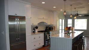A modern kitchen with white cabinetry, stainless steel appliances, a central island, and pendant lighting. - Shem Creek Paradise. Fish, Paddle, Kayak Off Your Own Covered dock with floater (Mt Pleasant)