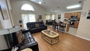 A living room with a sofa, a coffee table, and a dining area with chairs and a table. There is a kitchen area with cabinets and appliances. - 4BD/3B,EXECUTIVE VILLA WITH SPA,MUST SEE,10 MIN FROM DISNEY (Kissimmee)