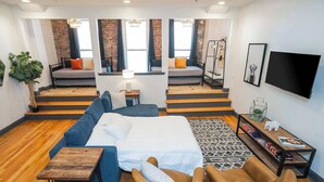A modern hotel room with a large bed, a sofa, a coffee table, and a TV. There are stairs leading to a balcony with a view. - On Broadway Above Boot Barn (Nashville)