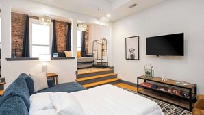A modern hotel room with a large bed, a sofa, a TV, and a staircase leading to an upper level. - On Broadway Above Boot Barn (Nashville)