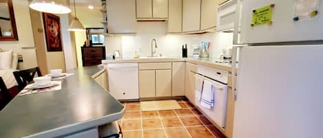 Cocina moderna con armarios blancos, lavavajillas integrado y refrigerador. Hay una isla de cocina con un fregadero y una lámpara colgante.