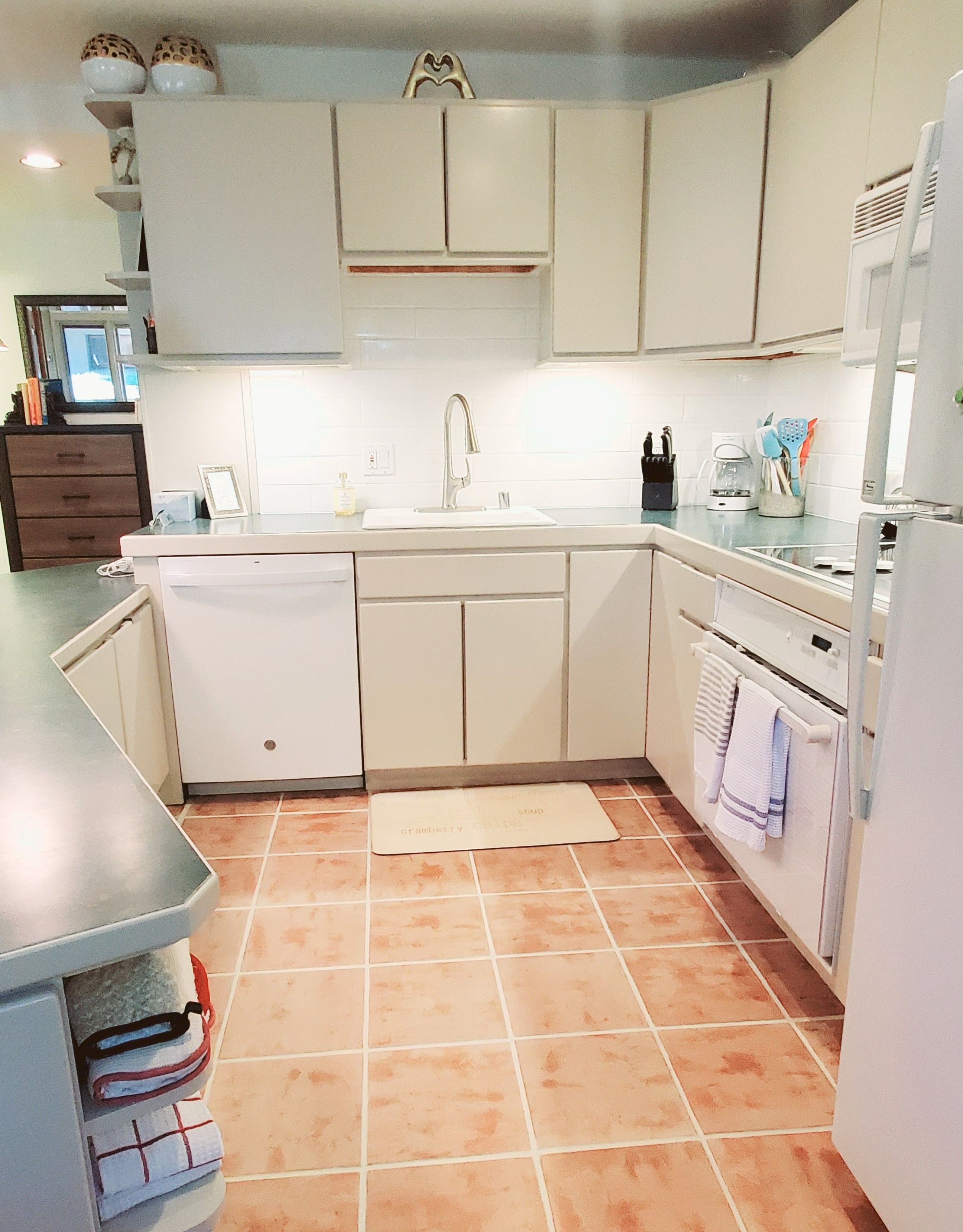 A kitchen with white cabinets, a stainless steel sink, and a tiled floor.