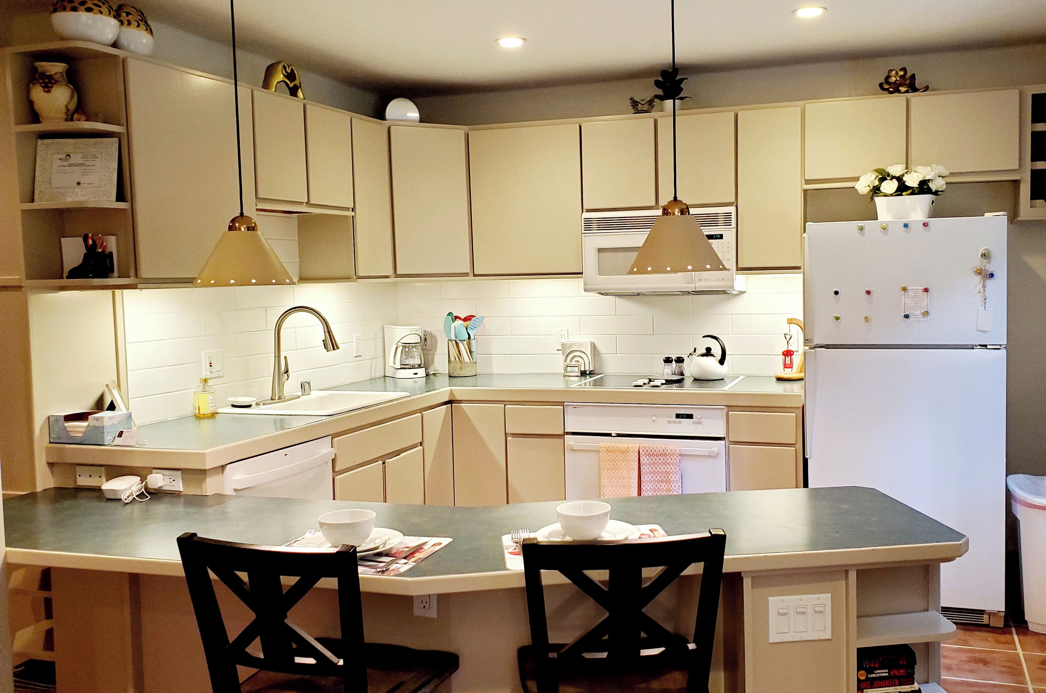 A kitchen with a central island, two chairs, a sink, a stove, and a refrigerator.