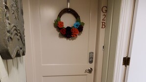 En vit dörr med en dekorativ krans, ett kodlås och en dörrmatta.