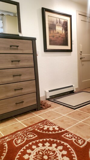 A room with a wooden dresser, a framed picture on the wall, a radiator, and a patterned rug.