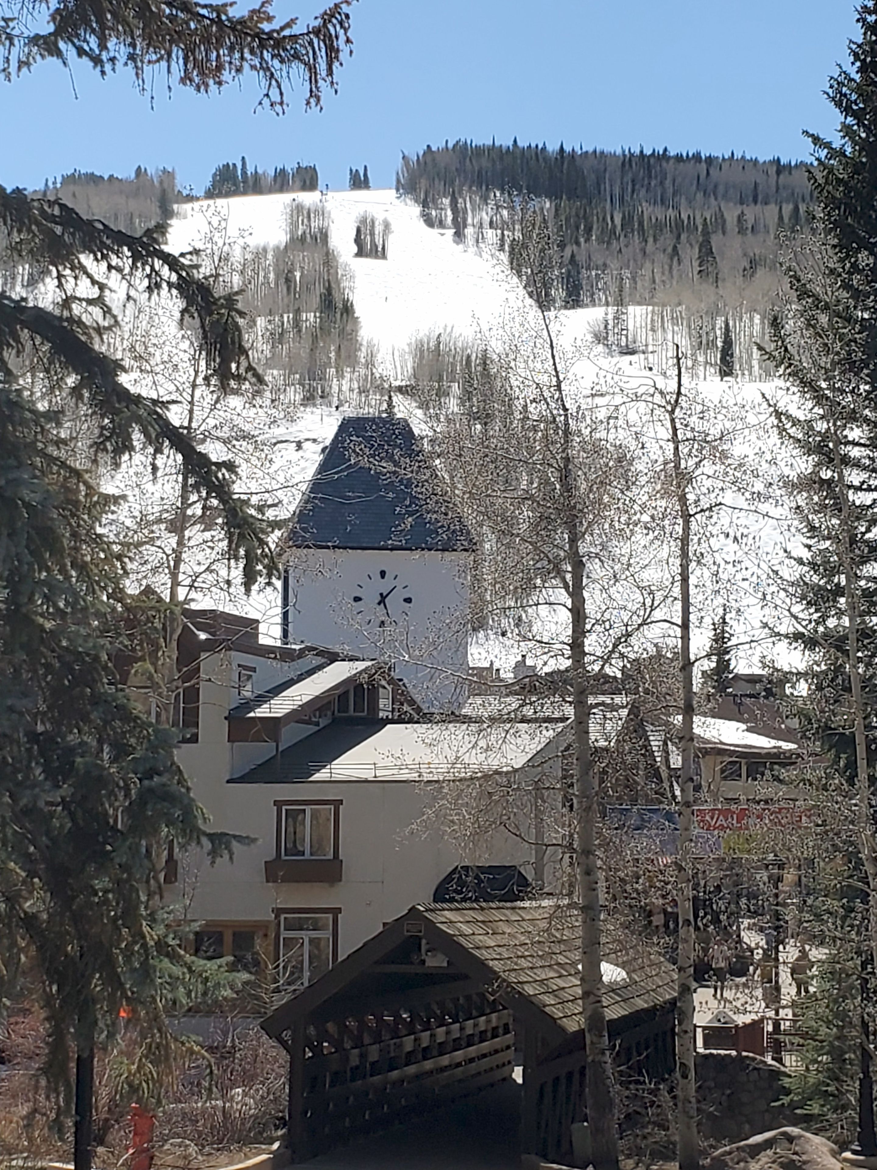 Ein Gebäude mit einem Glockenturm, umgeben von schneebedeckten Bäumen und wolkenlosem Himmel.