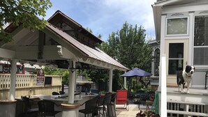 Un patio al aire libre con una zona de estar cubierta, una parrilla y un perro en el porche.