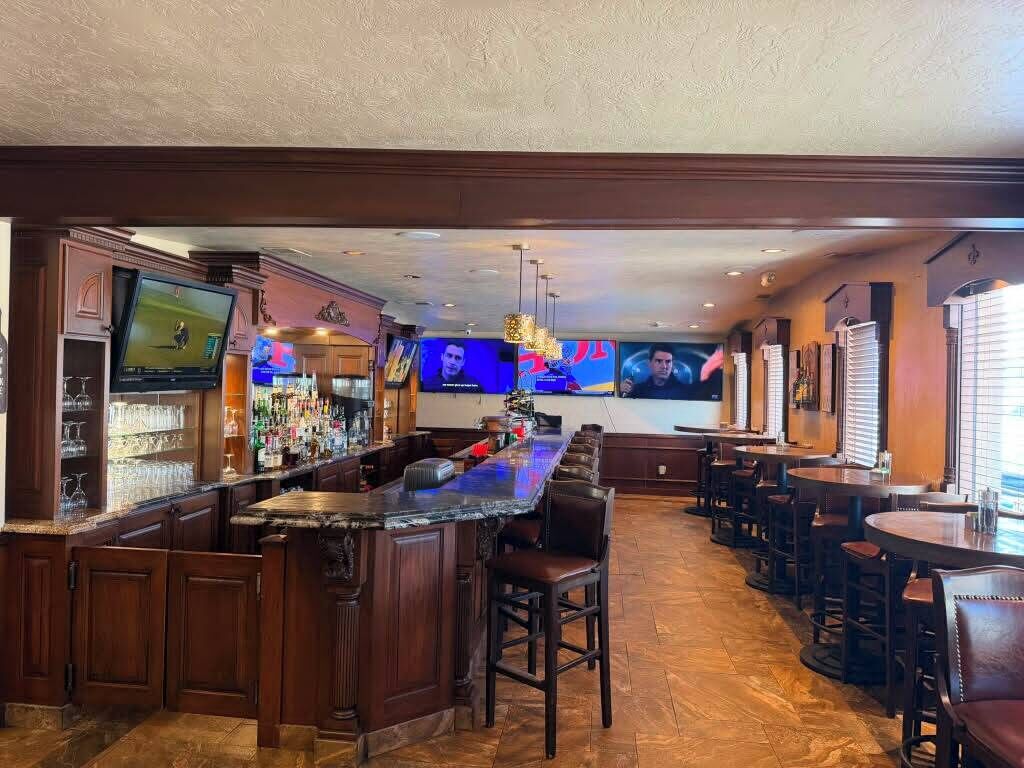 A bar area with a long counter, multiple stools, and televisions displaying sports.