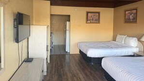 A hotel room with a bed, a TV, a refrigerator, and a door leading to a bathroom.