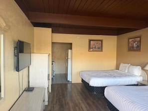 A hotel room with a bed, a TV, a refrigerator, and a door leading to a bathroom.