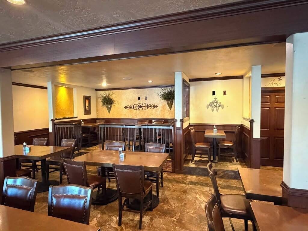 A restaurant with a marble floor, wooden tables and chairs, and decorative wall sconces.