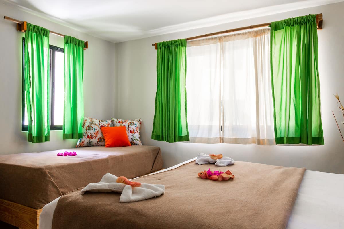 A hotel room with two beds, green curtains, a floral pillow, and towels on the beds.