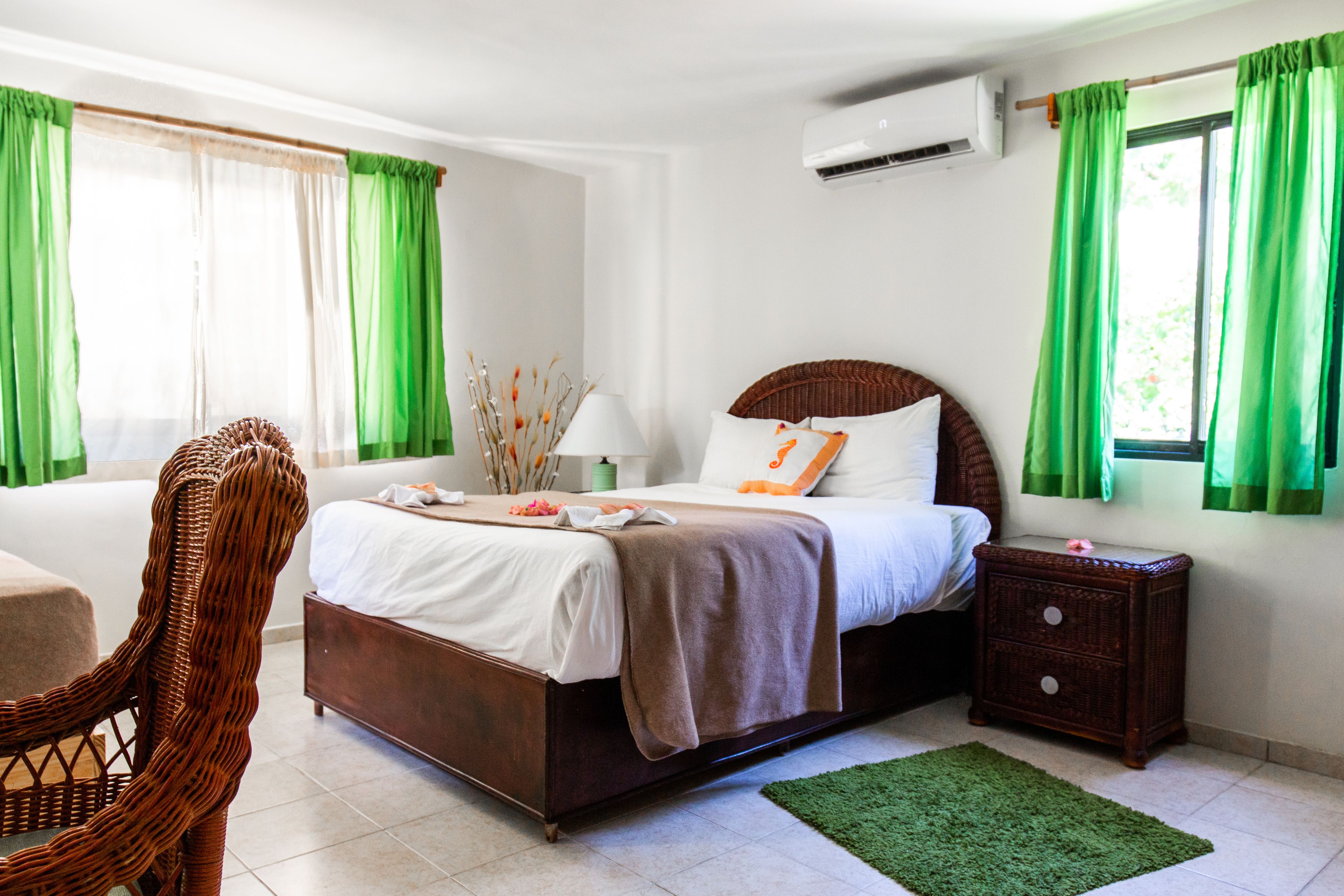 A bedroom with a bed, a chair, a nightstand, and a green rug.