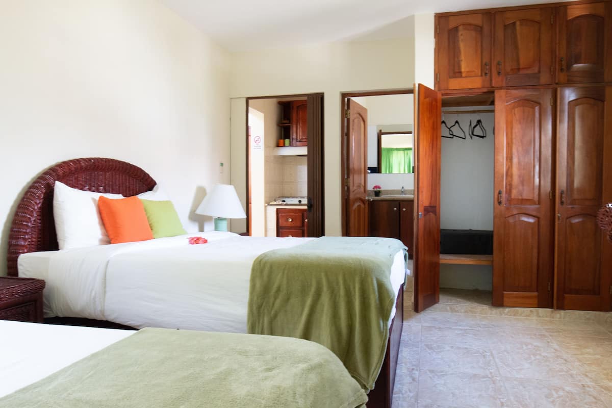 A hotel room with a bed, a nightstand, a lamp, a wardrobe, and a bathroom visible through an open door.