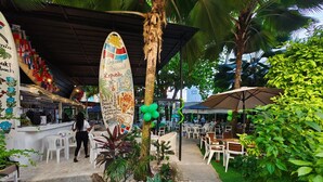 An outdoor dining area with white plastic chairs and tables, surrounded by greenery and a palm tree. - Riviera Punta Cana Eco Travelers House (Punta Cana)
