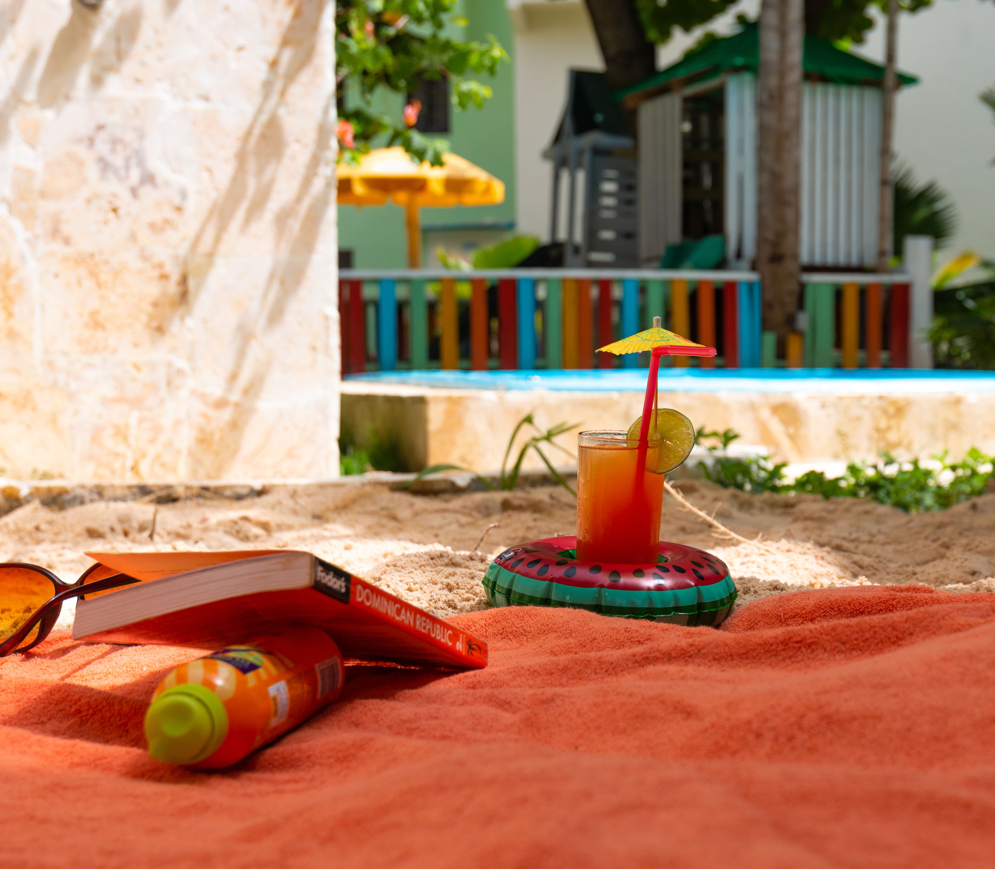 A beach setting with a drink, sunglasses, a book, and a beach umbrella.