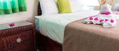 A neatly made bed with a green pillow, a wicker nightstand with a glass top, and a towel with pink flowers on a bed.
