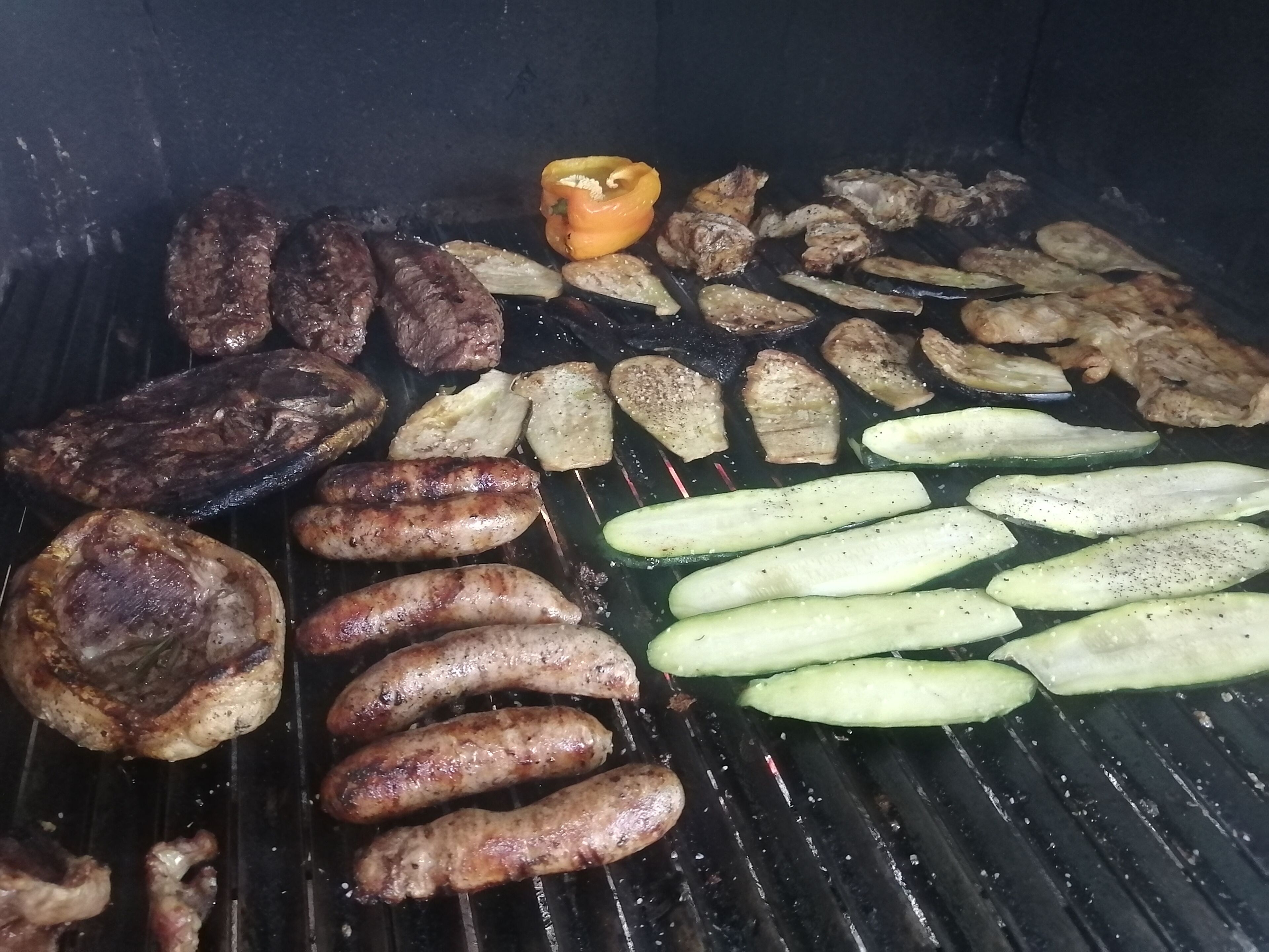 A grill with various meats and vegetables being cooked.