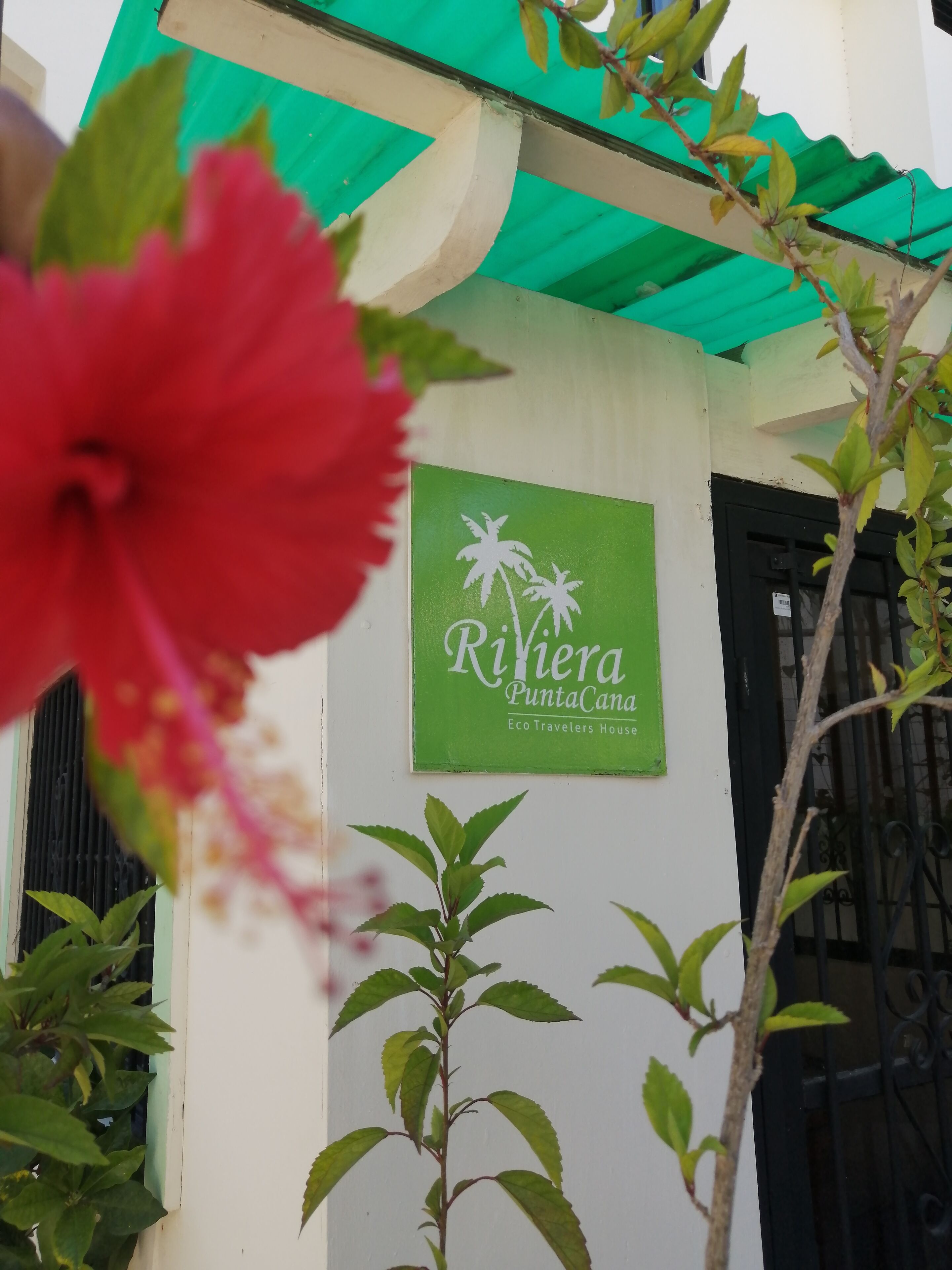 Un edificio con fachada verde y blanca, un letrero que dice "Riviera Punta Cana Eco Travelers House" y un portón negro.