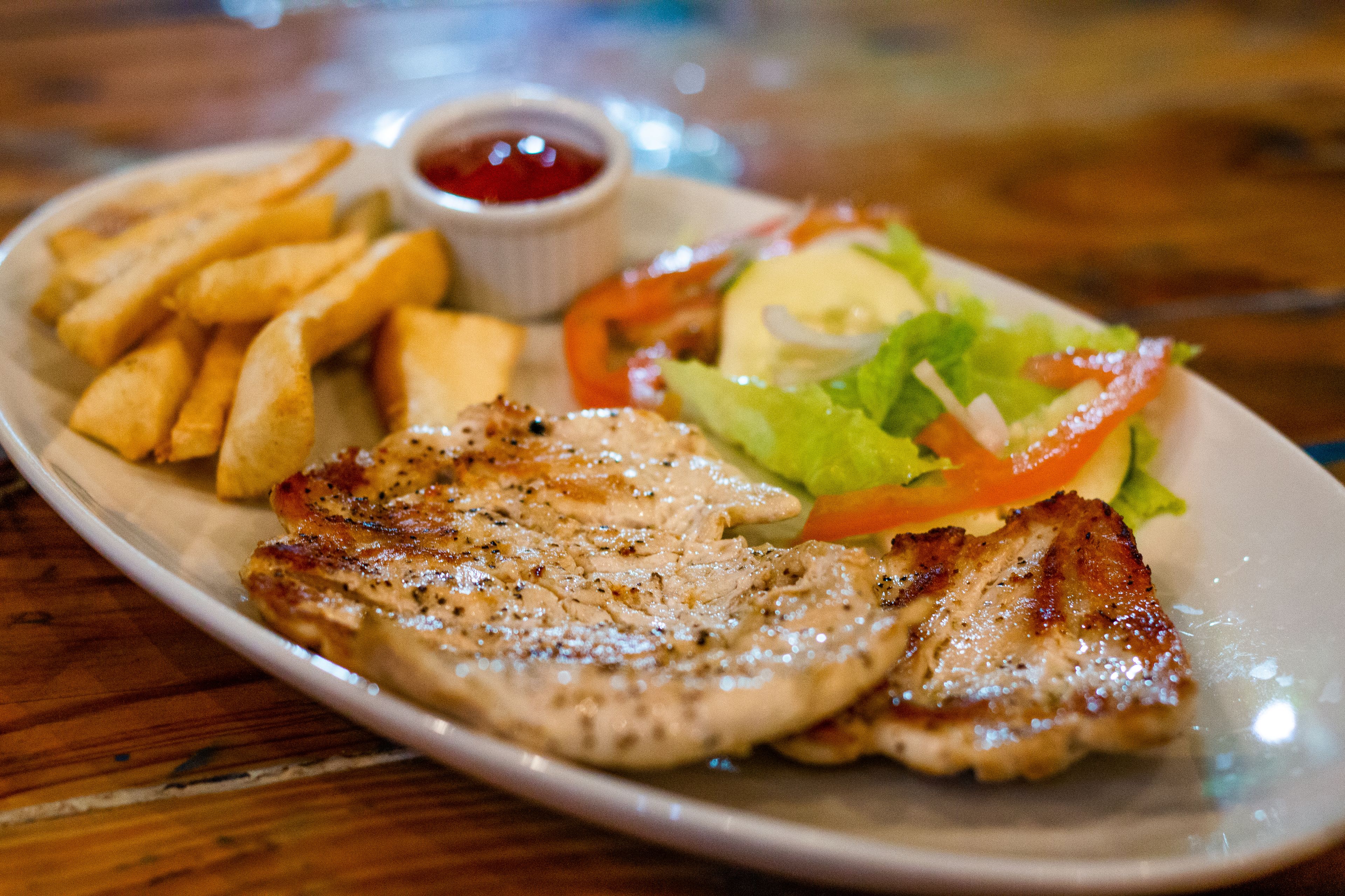 A plate with grilled pork, French fries, a salad, and a small bowl of ketchup.