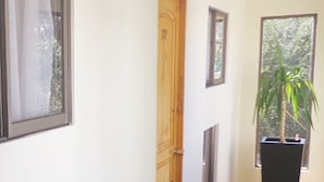 A hallway with a wooden door, a potted plant, and a window with a view of greenery. - Hotel Pulmahue (Copiapó)