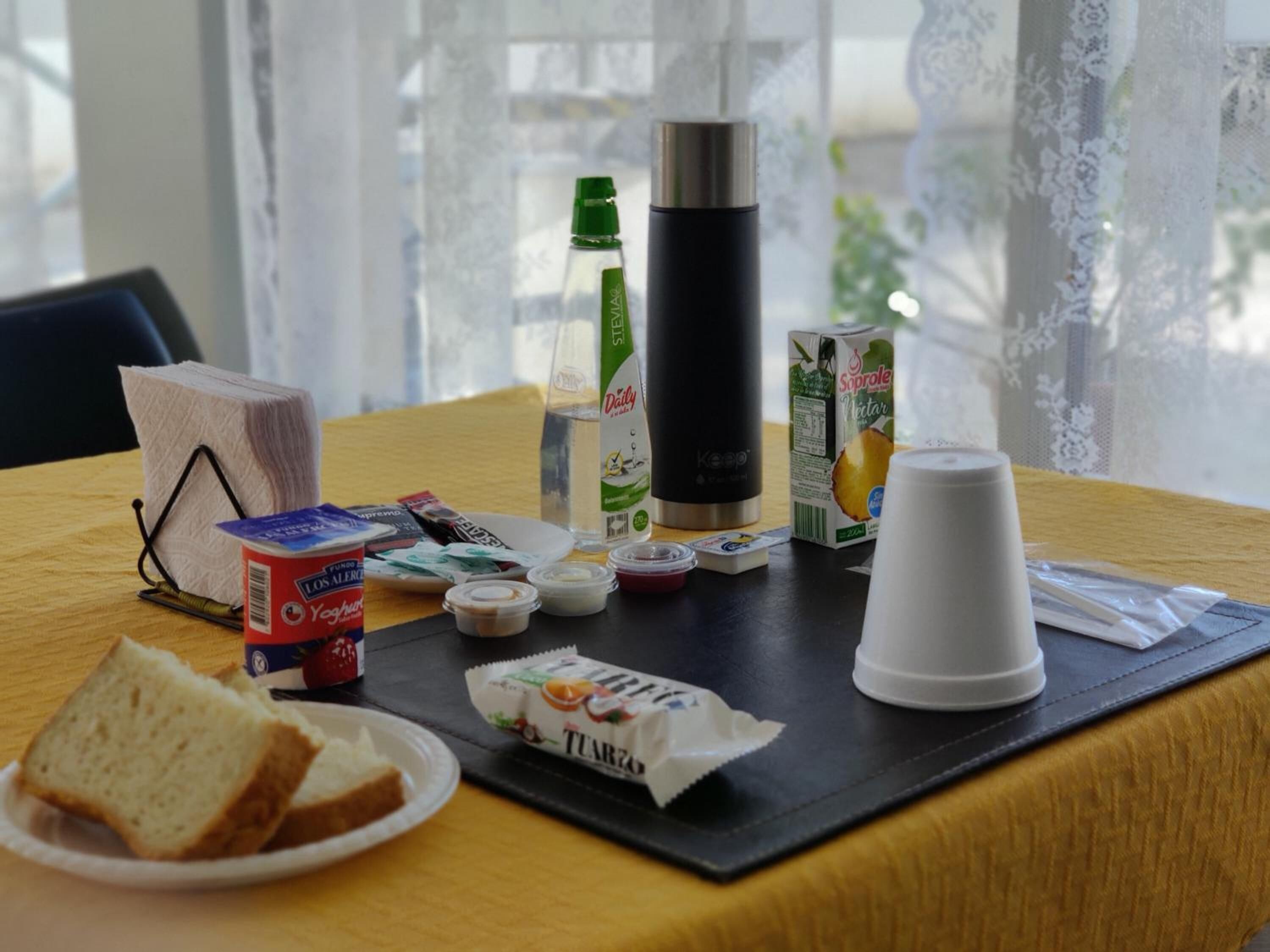 Desayuno con pan, jugo, café y aderezos sobre una mesa.