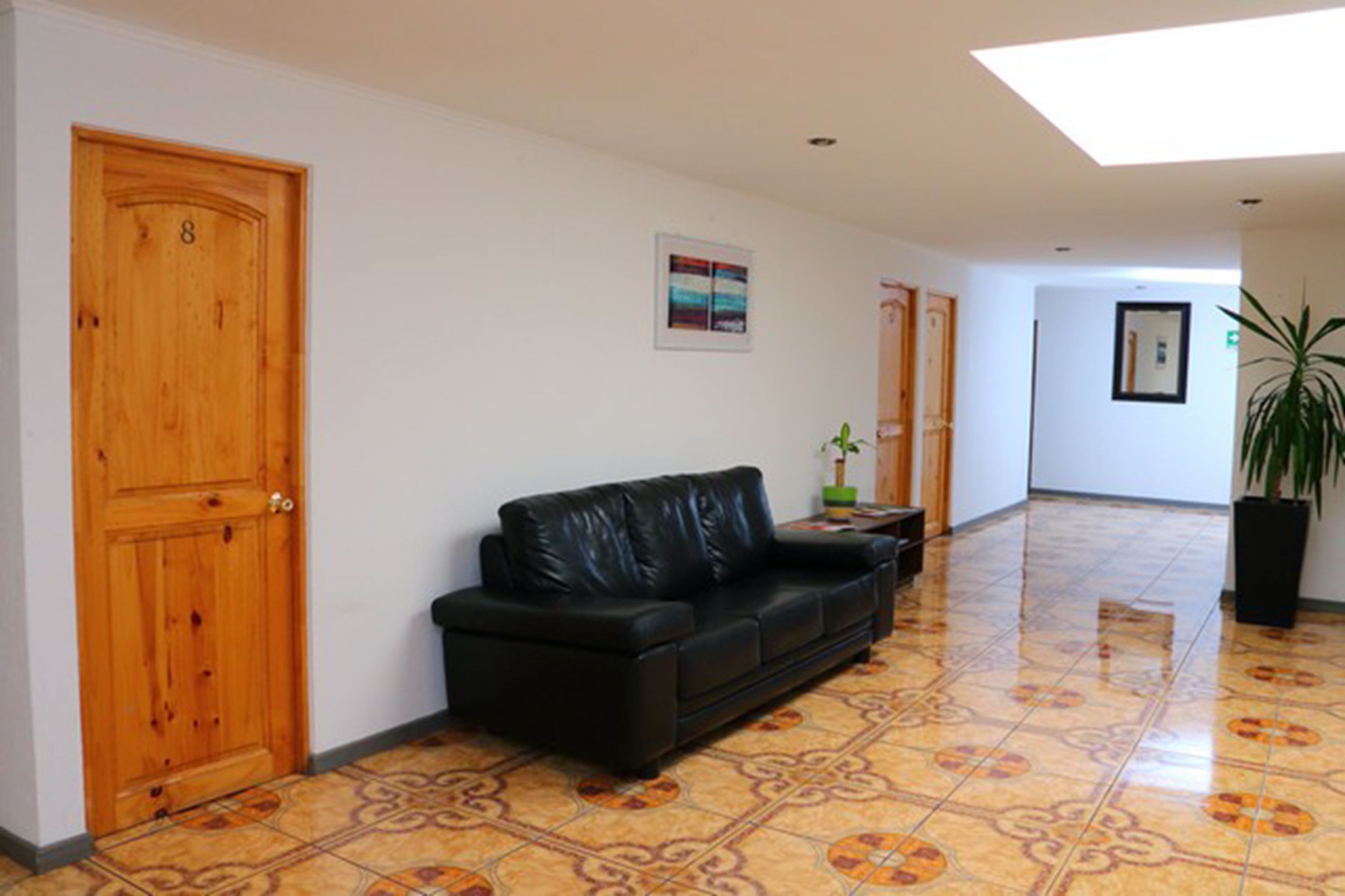 A hallway with a black leather sofa, wooden doors, and a tiled floor.