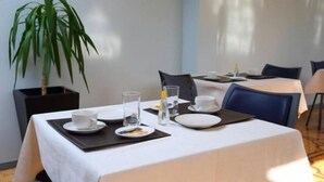 A dining area with a table set for two, including plates, glasses, and cutlery. There is a potted plant to the left of the table. - Hotel Pulmahue (Copiapó)