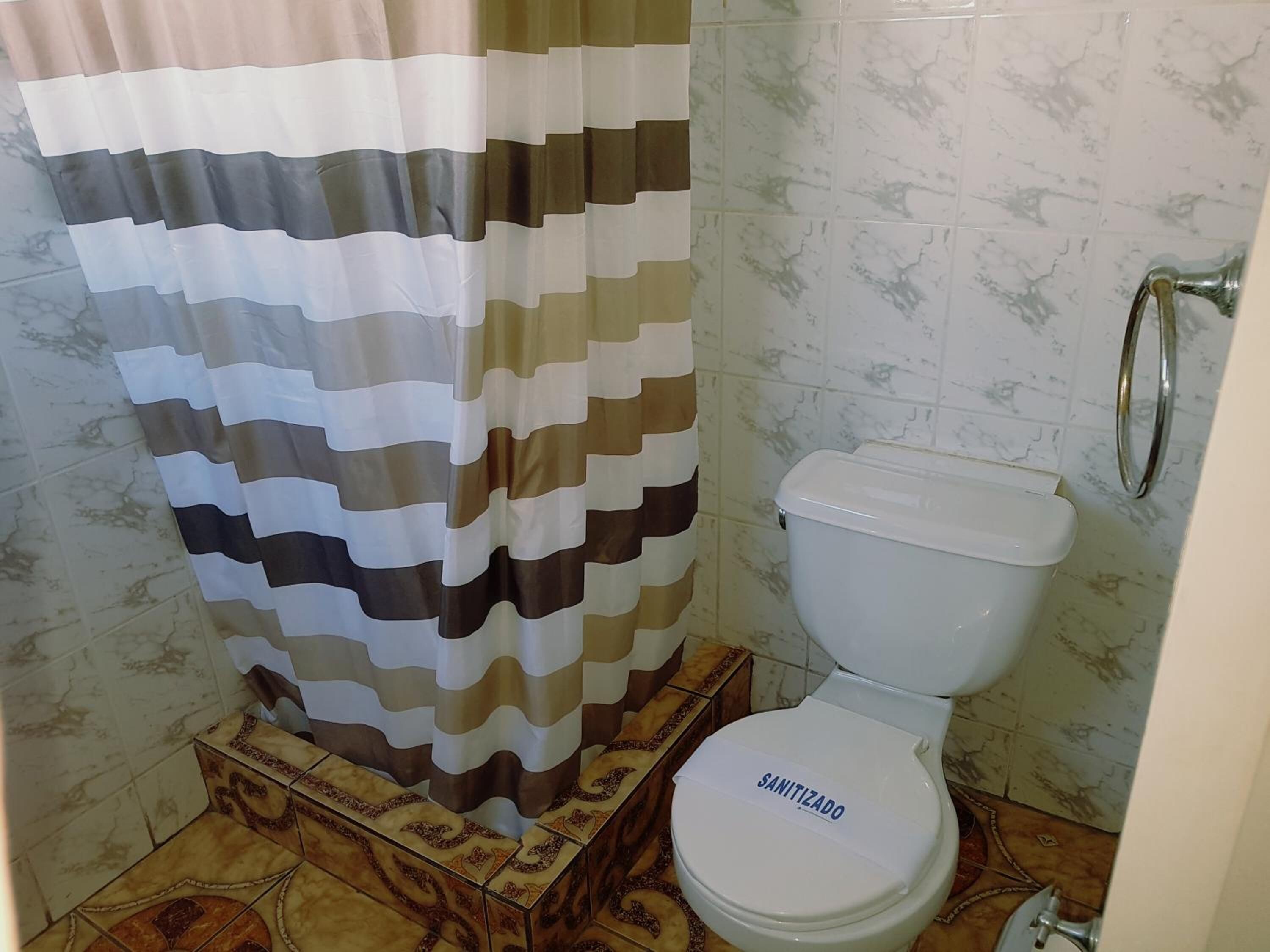 Un baño con cortina de ducha a rayas, un inodoro con letrero que dice 'SANITIZADO' y baldosas estampadas.