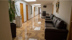 A hallway with a patterned floor, a sofa, a refrigerator, and a plant. - Hotel Pulmahue (Copiapó)