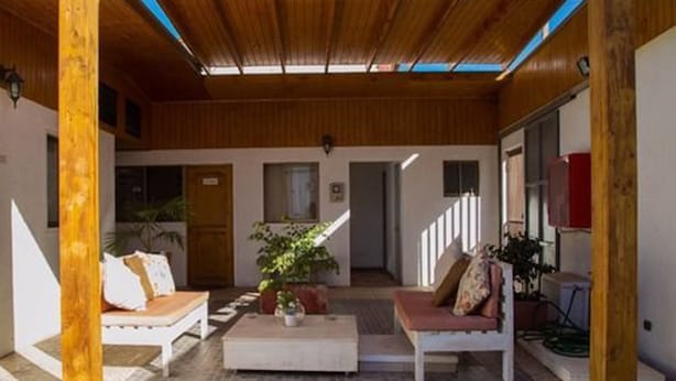 A covered outdoor area with wooden beams, two white sofas with cushions, a coffee table, and potted plants. - Hotel Pulmahue (Copiapó)