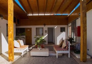 Un espace extérieur abrité, doté de poutres en bois, de deux canapés blancs avec des coussins, d’une table basse et de plantes en pot.