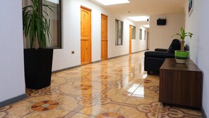 A hallway with a tiled floor, wooden doors, a black bench, and a potted plant. - Hotel Pulmahue (Copiapó)