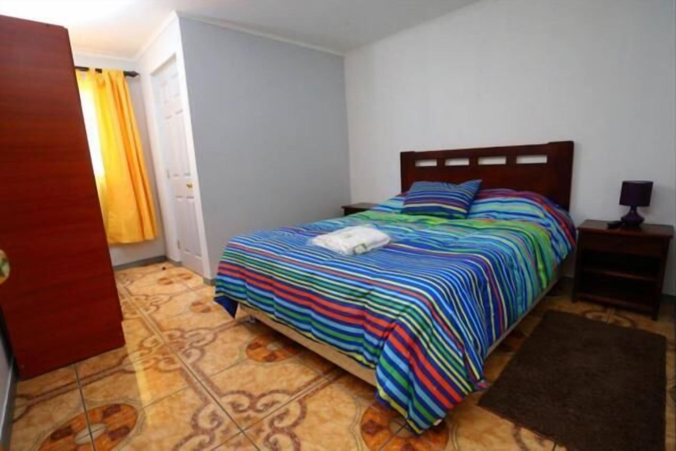 A bedroom with a bed, a nightstand, a wooden wardrobe, and a bathroom door.
