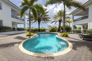 A swimming pool surrounded by palm trees and a white building with balconies. - Palm Crest (Jan Thiel)