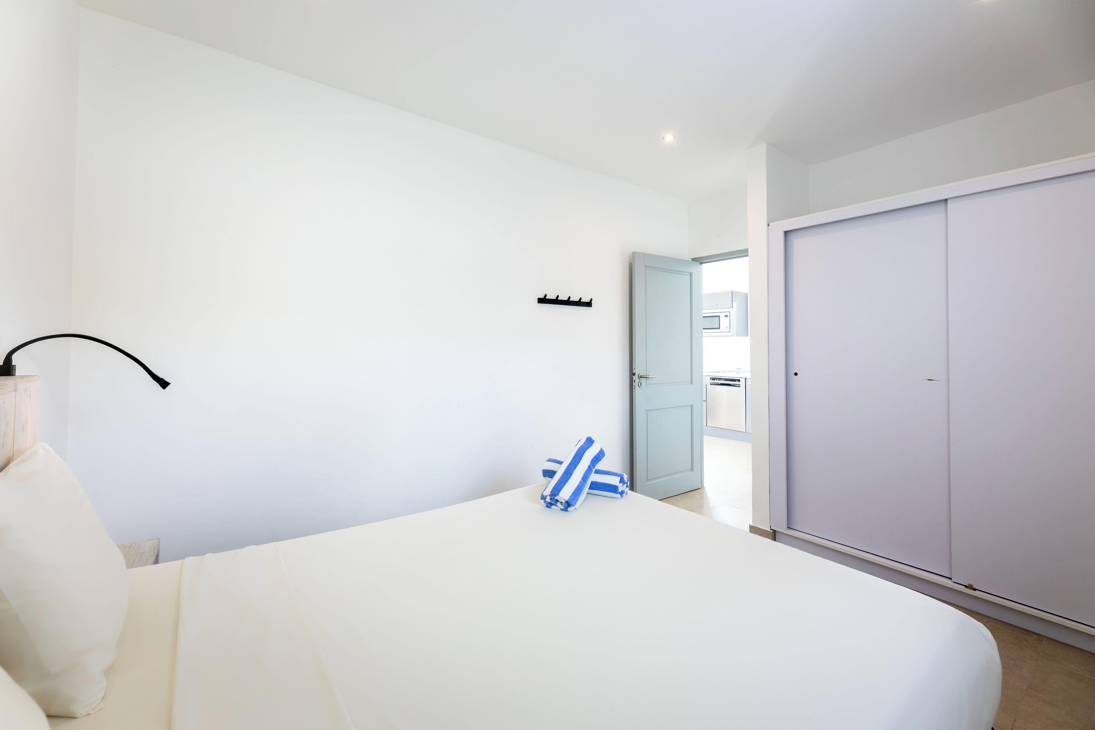 Une chambre à coucher comprenant un lit, une table de chevet, une lampe, une armoire et une porte donnant sur une autre pièce.