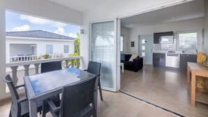 Une cuisine moderne équipée d’un four à micro-ondes, un coin repas avec une table et des chaises, et une porte-fenêtre coulissante donnant sur un balcon.