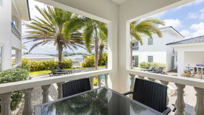 Un balcon avec une table et des chaises en verre, donnant sur une piscine et des palmiers.