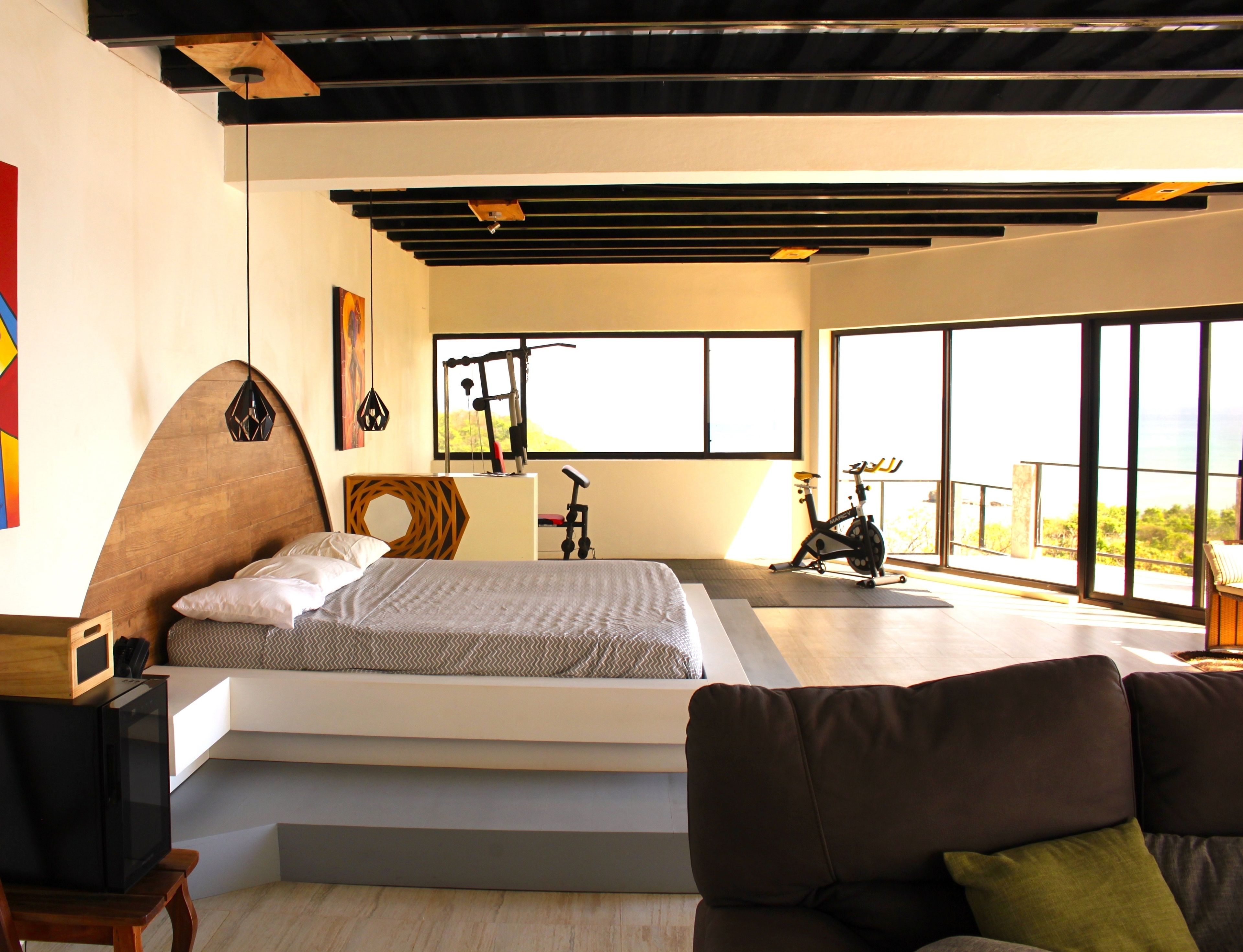 A modern bedroom with a large bed, a bike, and a view of the outdoors.