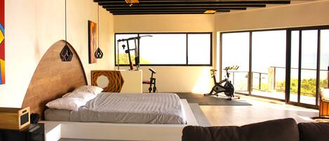 A modern bedroom with a large bed, a bike, and a view of the outdoors.