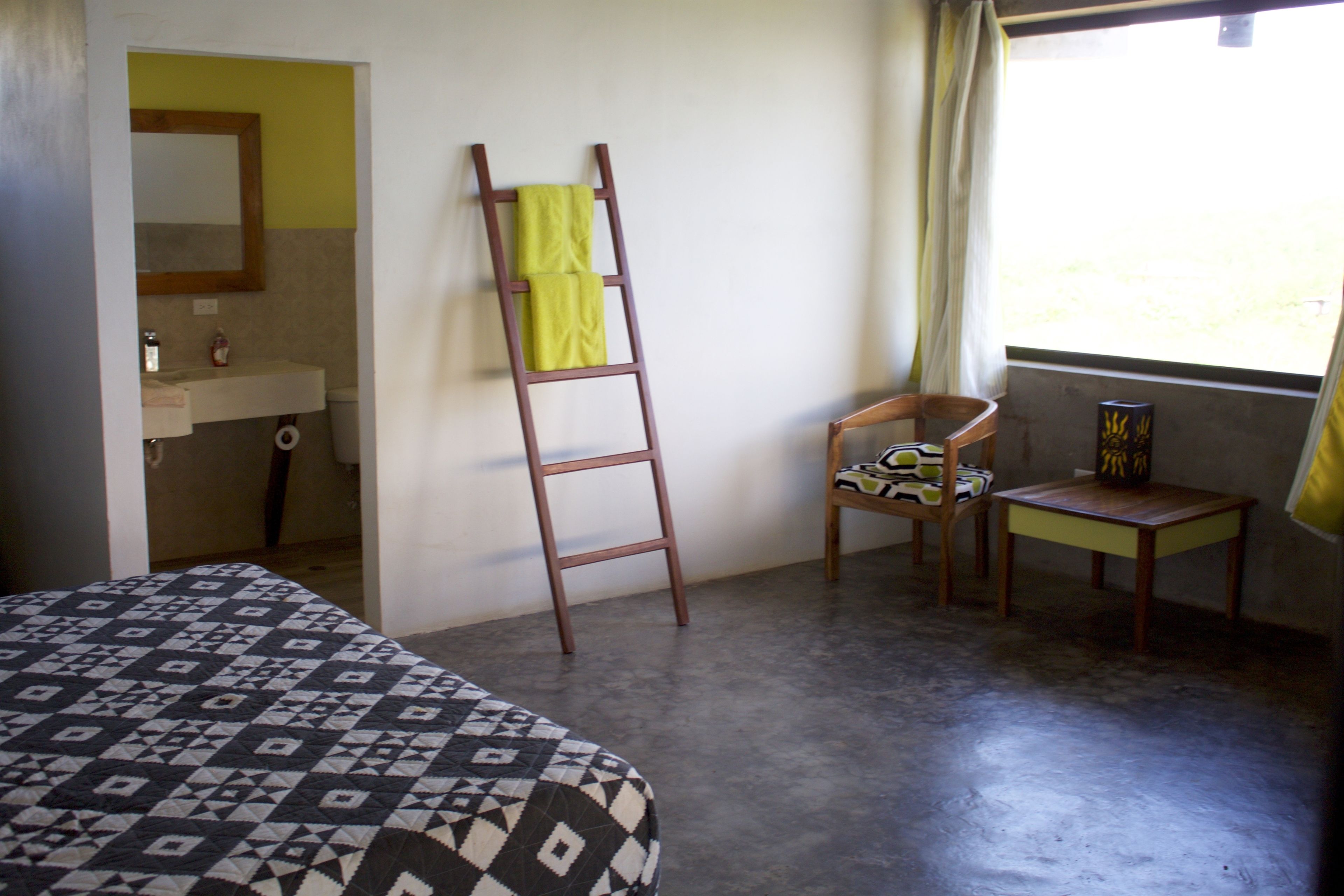 A bedroom with a bed, a wooden ladder, a chair, a small table, and a window with curtains.