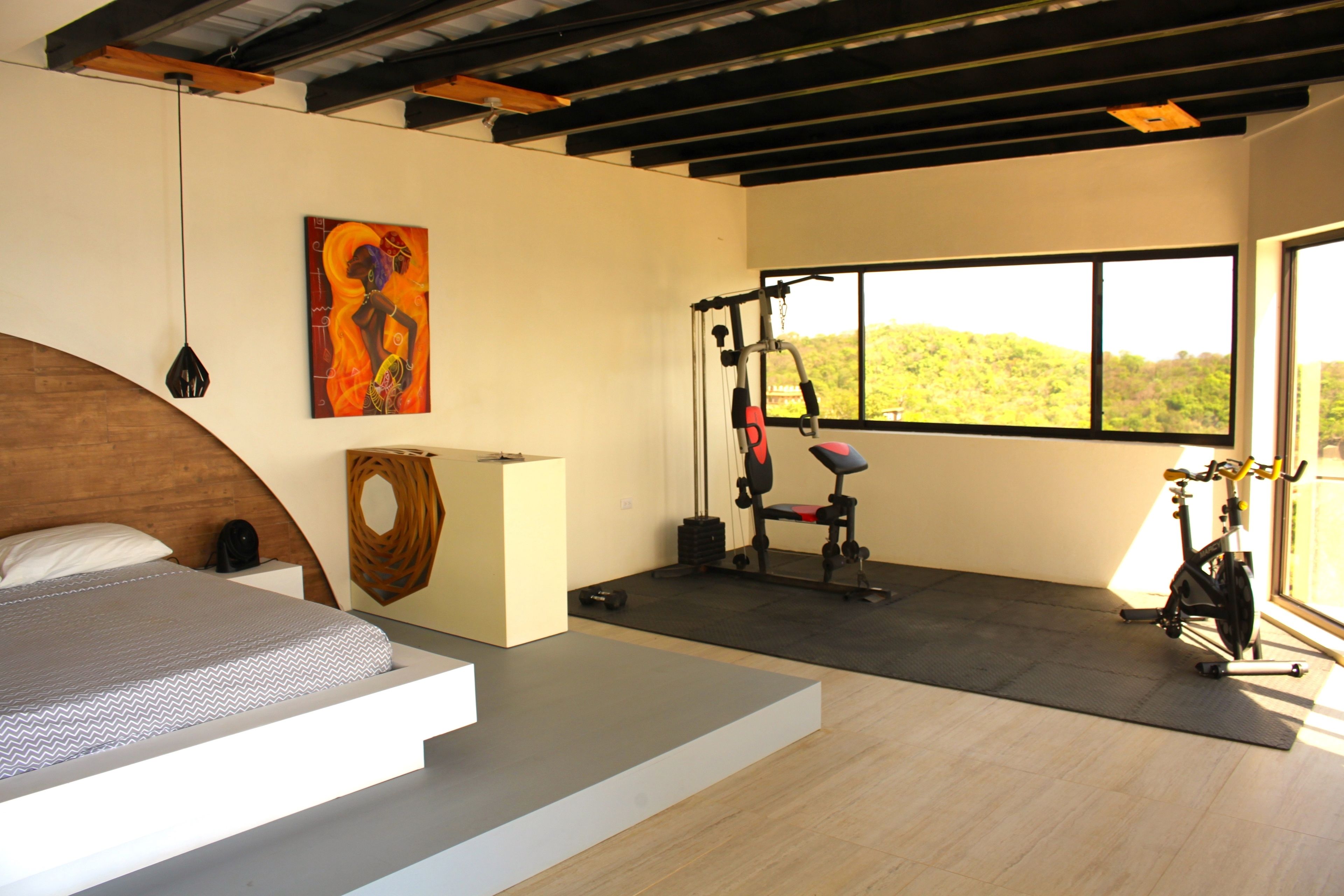 Quarto moderno com cama, espaço para exercícios e uma grande janela com vista para colinas.